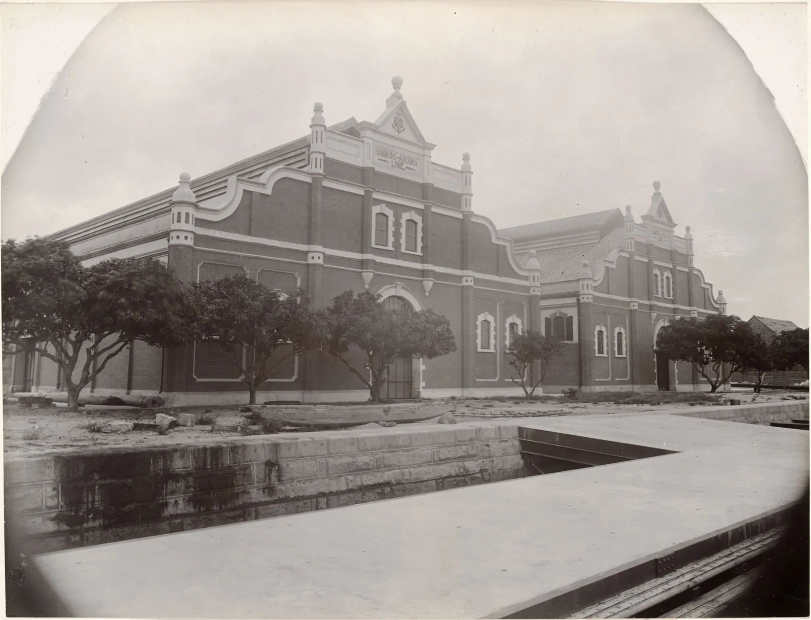 Two large brick warehouses with curved Dutch gables beside a stone embankment.